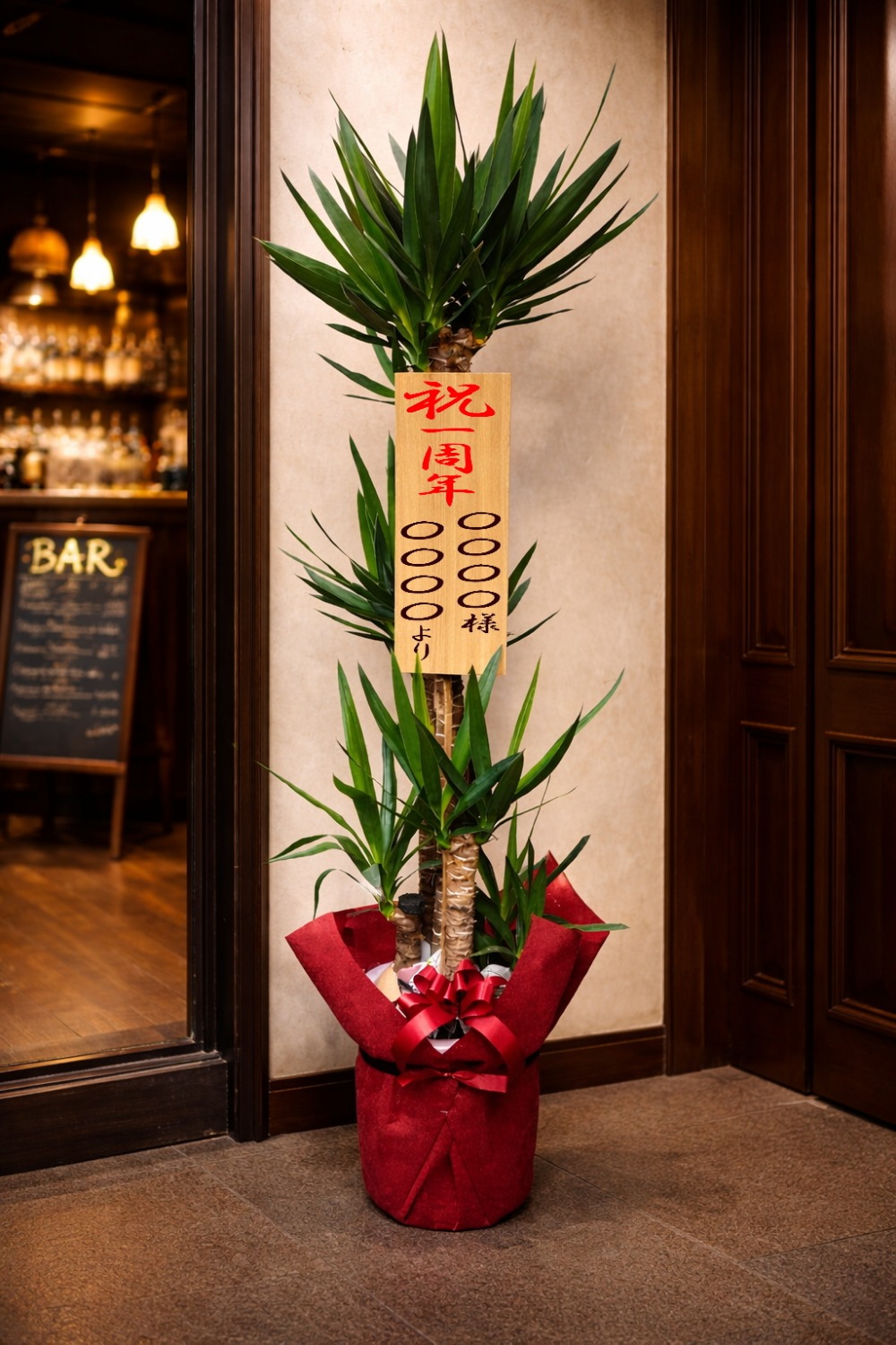 一周年祝の立札を付けた観葉植物ユッカ10号鉢の設置イメージ画像（BARの店先）